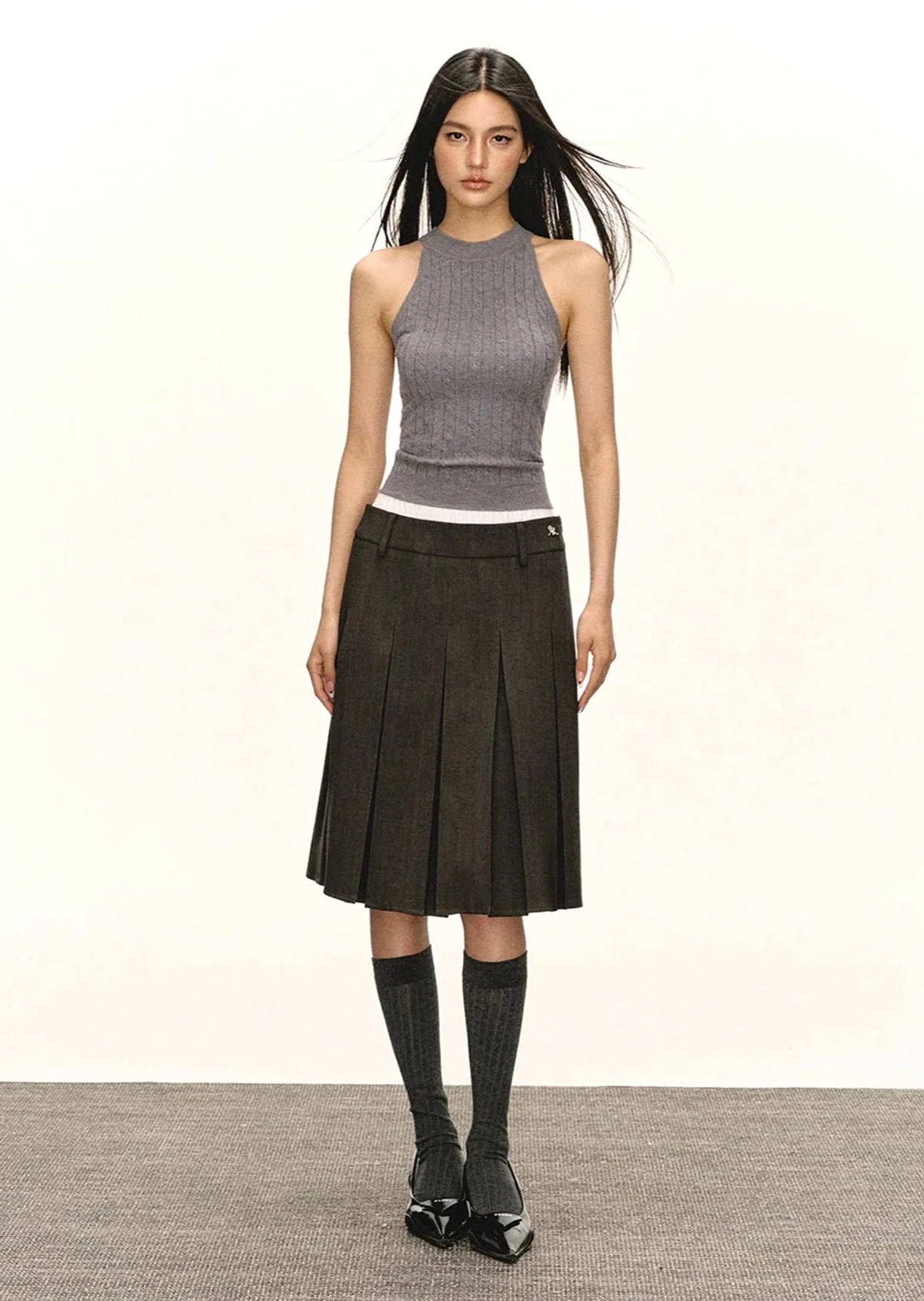 Dark grey sleeveless cropped mock neck knit top styled with pleated midi skirt knee-high socks and leather loafers