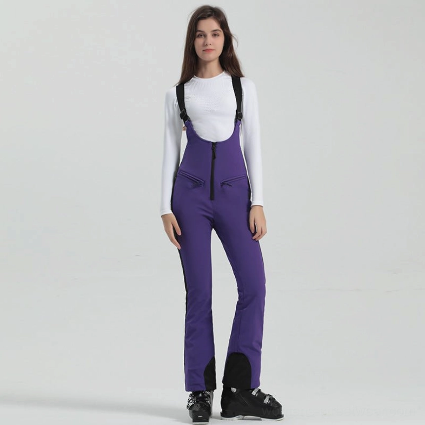 Women's deep purple slim flared bib ski overalls with black ankle cuffs, adjustable shoulder straps, front zipper, and ski boots
