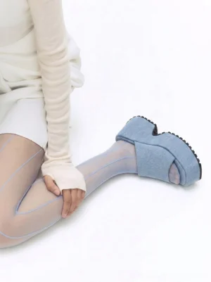 Woman wearing light blue denim platform slide sandals with sheer blue stockings, white top, and white shorts
