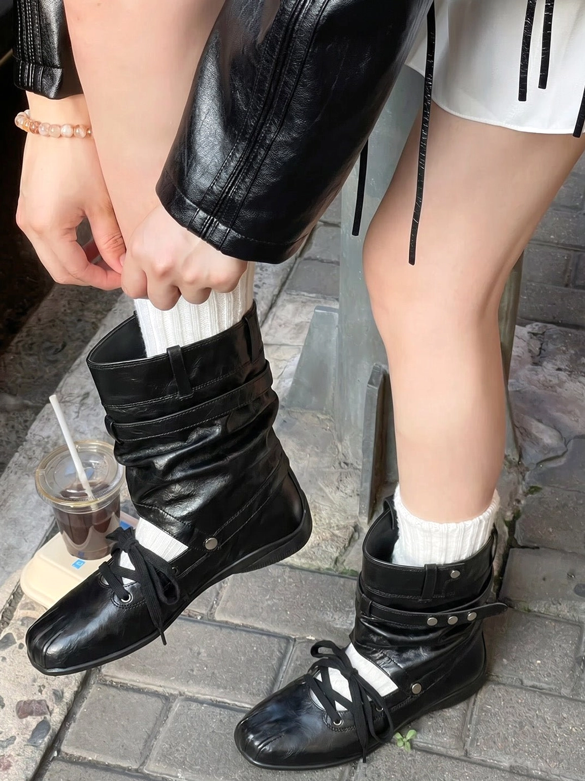 Close-up street style view of women's black square-toe utility boots with layered straps and cutout shaft