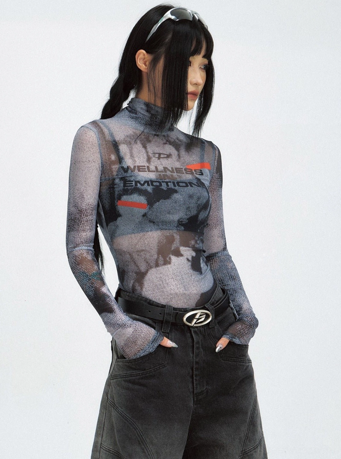 Side view of a women's fitted sheer mesh long-sleeve turtleneck top styled with black wide-leg denim and a silver belt