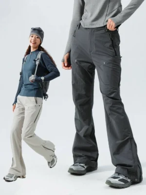 Women wearing flared outdoor performance pants with hiking backpacks on a trail, showing the technical streetwear silhouette and utility pocket design