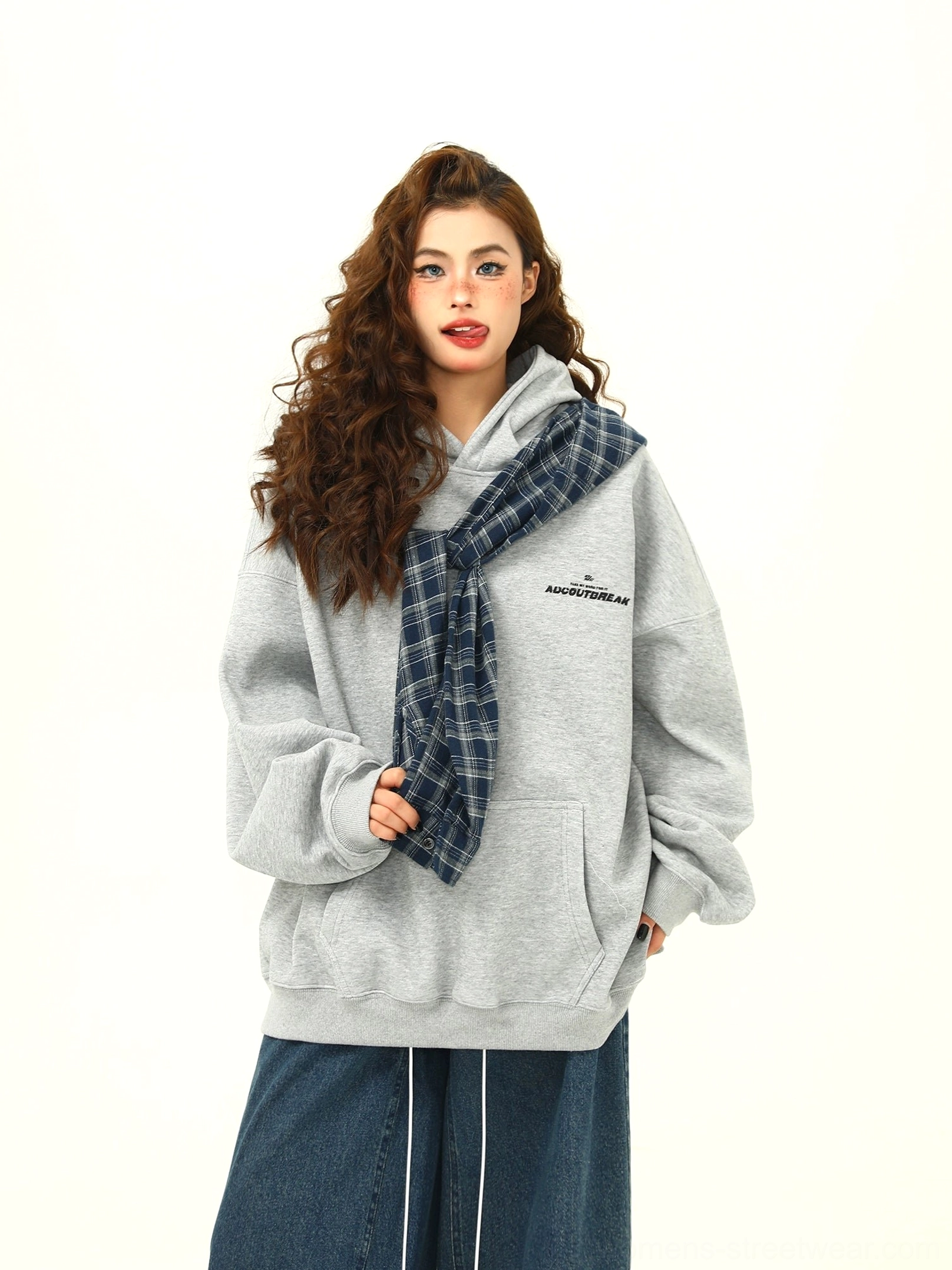 Close-up front view of an oversized women’s grey plaid hoodie showing the kangaroo pocket, subtle chest print, and blue plaid scarf-inspired hood accent