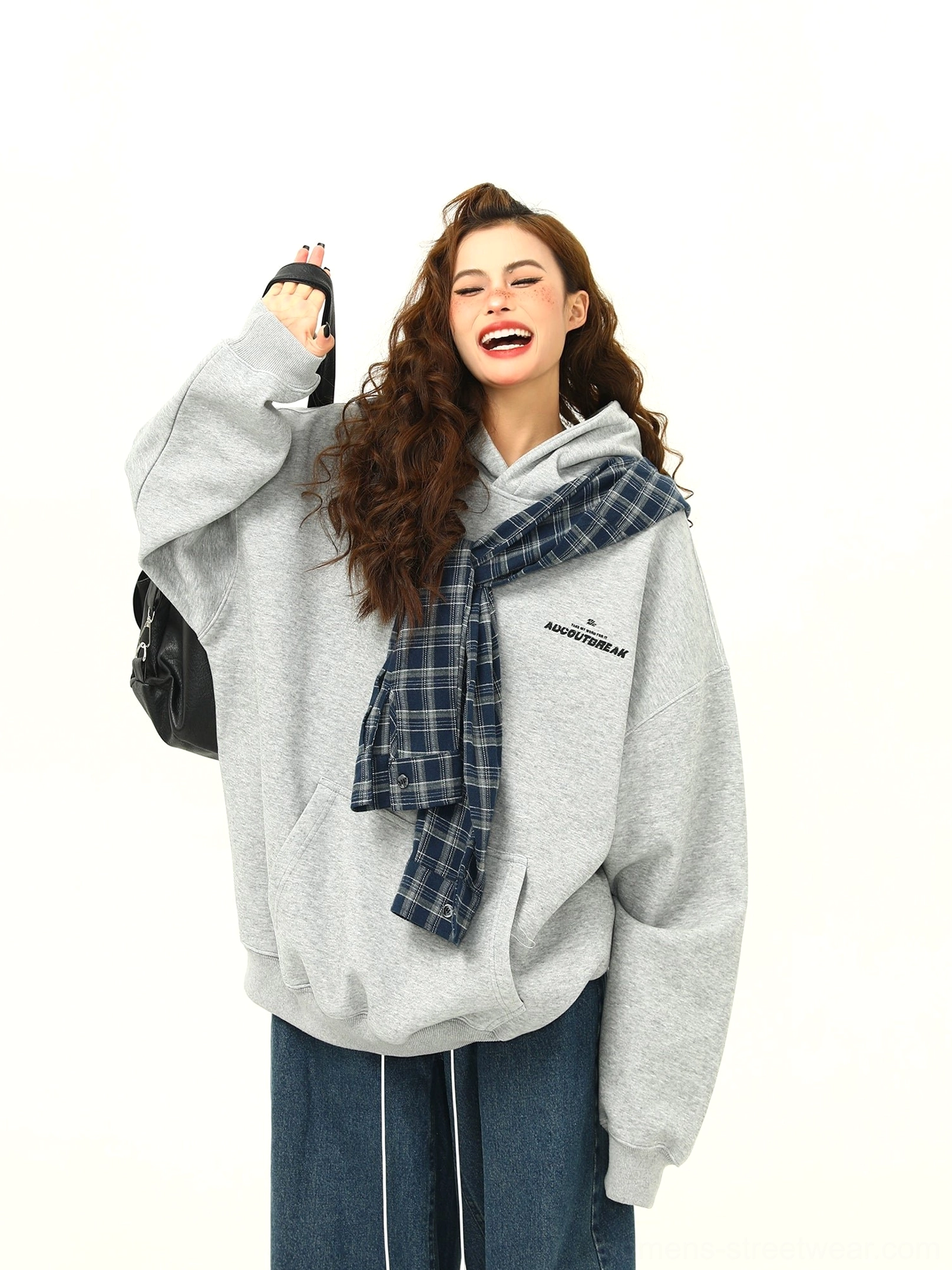 Smiling female model wearing an oversized heather grey plaid accent hoodie with blue plaid hood detail, wide-leg jeans, shoulder bag, and casual Seoul street style