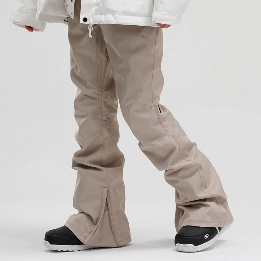 Khaki women's flared snow pants with matte technical outdoor fabric, side ankle zipper, black and white ski boots, and off-white jacket