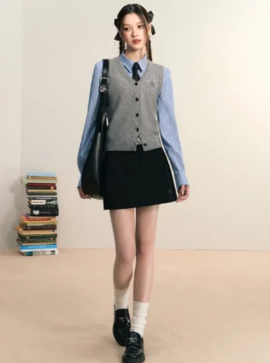 Women's blue striped button down shirt layered under a grey knit vest with black mini skirt in Korean preppy streetwear outfit
