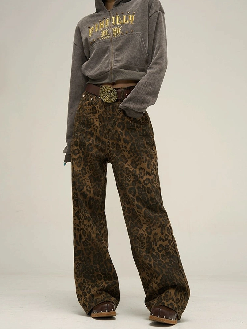 Front view of women's brown and black leopard print wide leg streetwear pants styled with a grey zip-up hoodie, brown belt, and leather clogs