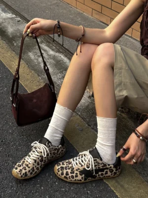 Women's leopard print low-profile retro trainers worn with ruffle socks on an urban street while adjusting cream laces