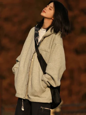 Women wearing a loose light gray plaid-lined hooded jacket with snap buttons, white tee, black crossbody bag, and roomy pockets