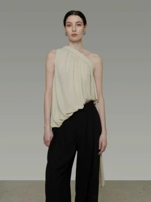 Light green apricot asymmetric one-shoulder drape tie tank top styled with black wide-leg trousers in a studio