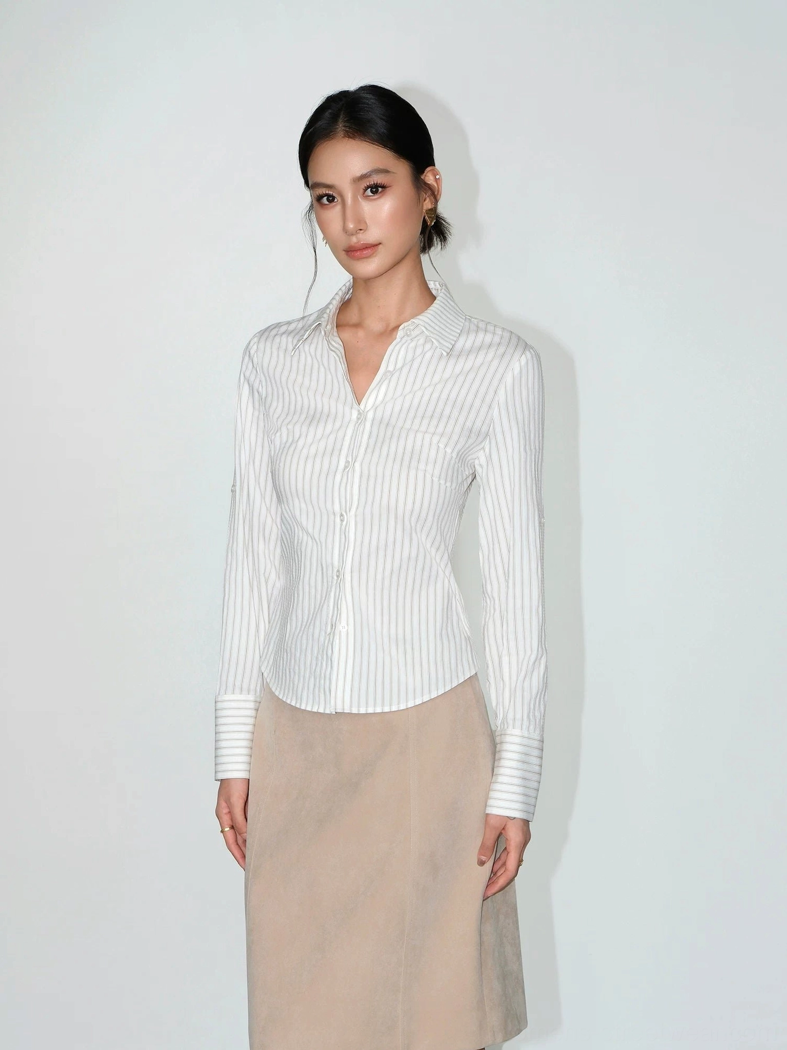 Full-body view of a women's long-sleeve pinstripe tailored shirt with slim silhouette styled with a beige midi skirt