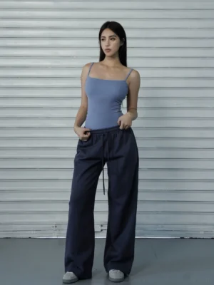 Women’s dark navy low-rise drawstring wide-leg streetwear pants styled with a light blue camisole in a studio front view