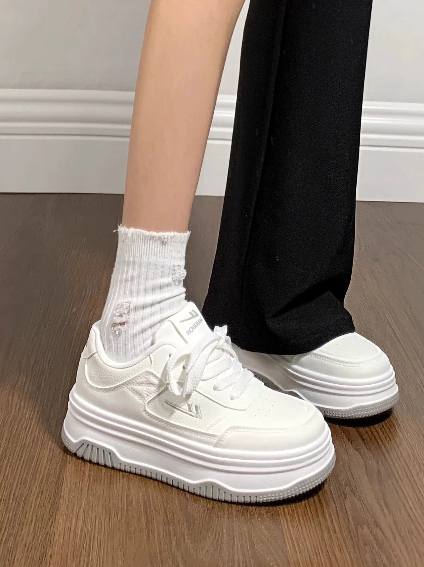 Women's minimalist all-white chunky platform sneakers worn with black flare pants and white crew socks