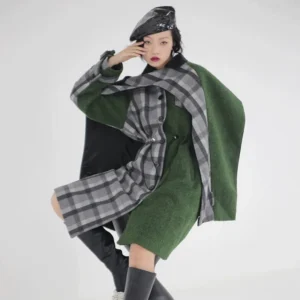 Women's moss green and grey plaid hybrid cape coat shown in a three-quarter studio view with asymmetric layered panels, relaxed silhouette, patent beret, and black knee-high boots