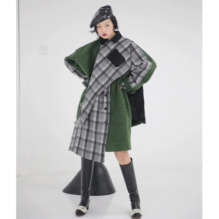 Front full-body view of women's moss green hybrid coat with grey plaid wrap overlay, asymmetric cape panels, drawstring waist, and black heeled knee-high boots