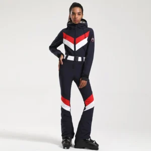 Women's navy blue one-piece ski suit with red and white chevron chest panels, striped flared ski pants, adjustable hood, and black ski boots