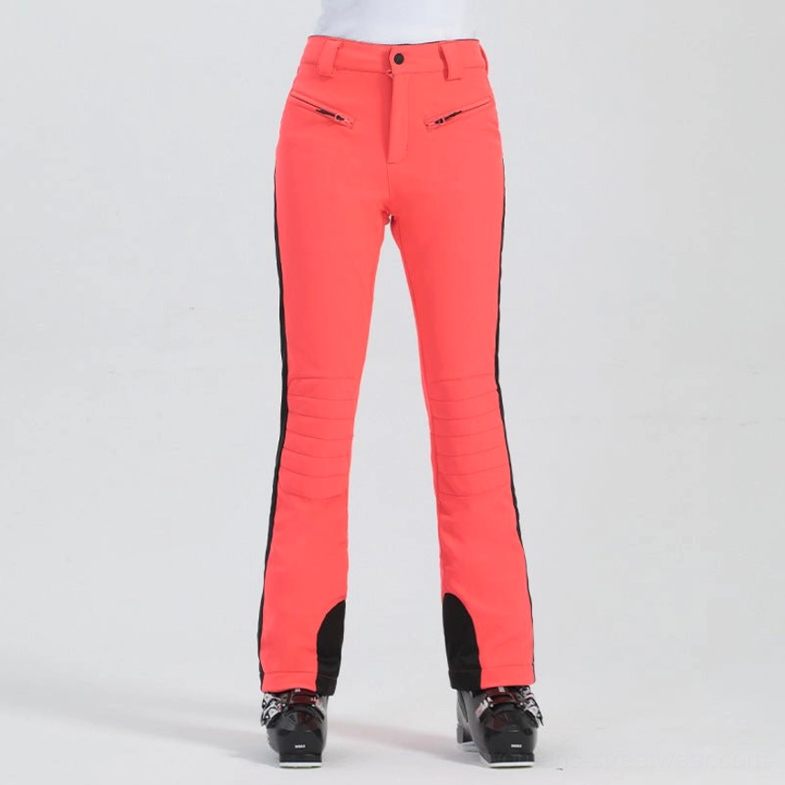Bright orange red women's technical ski pants with black side stripes, shaped knees, flared cuffs, and resort streetwear look