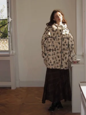 Women's oversized floral sherpa hooded jacket with contrast piping styled with a dark plaid midi skirt indoors