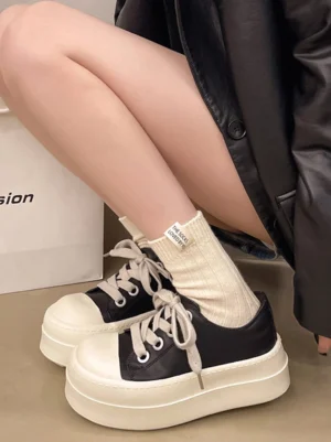 Women's black and white oversized toe low top platform sneakers worn with beige letter crew socks in indoor streetwear styling