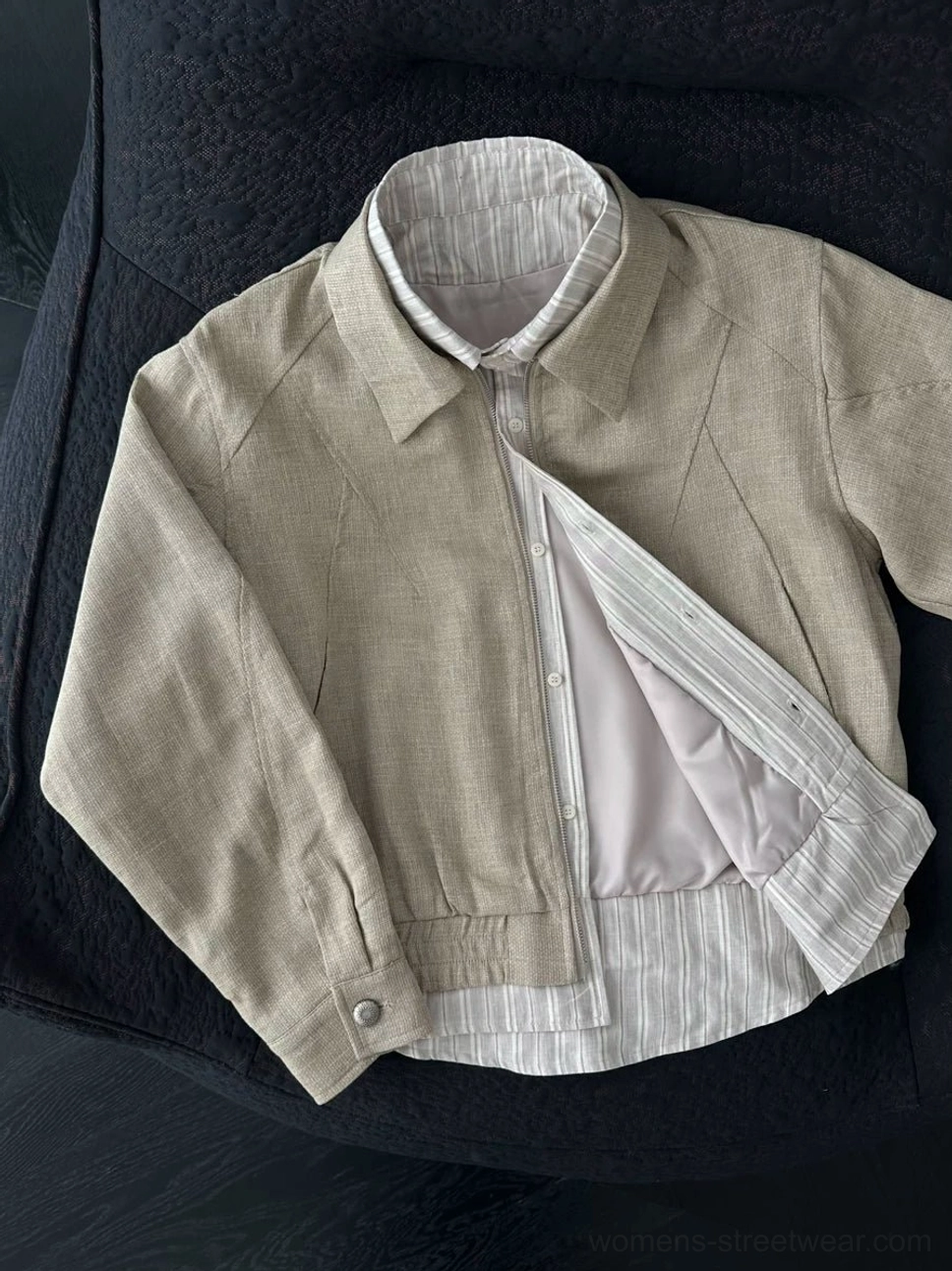 Oblique view of a partially unzipped women's cropped linen blend jacket revealing the striped shirt layer, soft lining, snap details, and relaxed fit