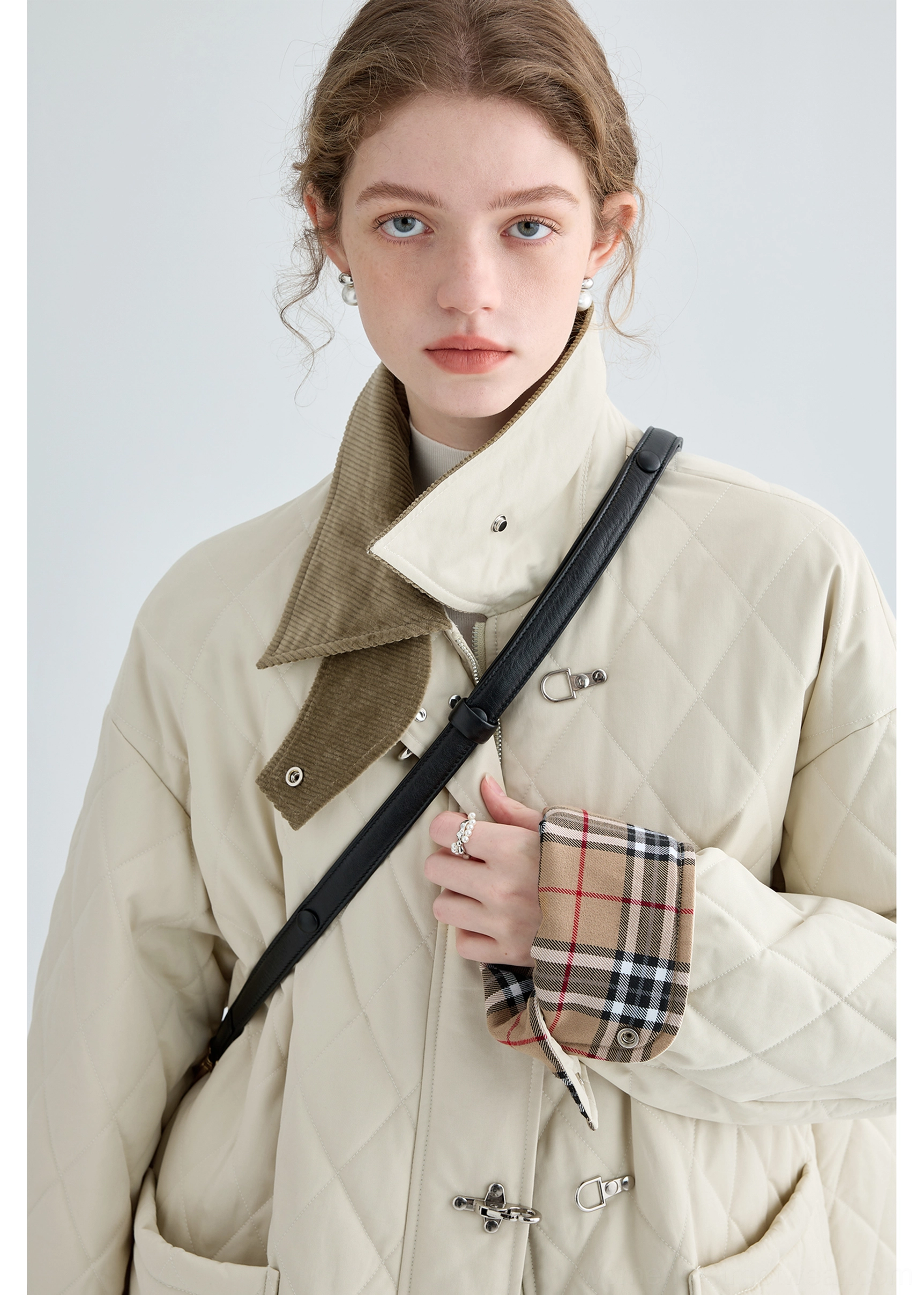 Close-up of beige diamond quilting, brown corduroy collar, plaid cuff lining and metal buckle closure on women's cotton jacket