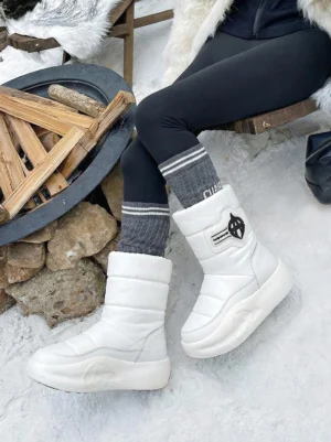 White padded mid-calf platform snow boots worn with black leggings and grey crew socks in a snowy winter setting