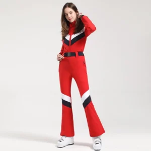 Women's red one-piece ski jumpsuit with black white and red chevron color blocking, flared snow pants, wide black waist belt, and white ski boots