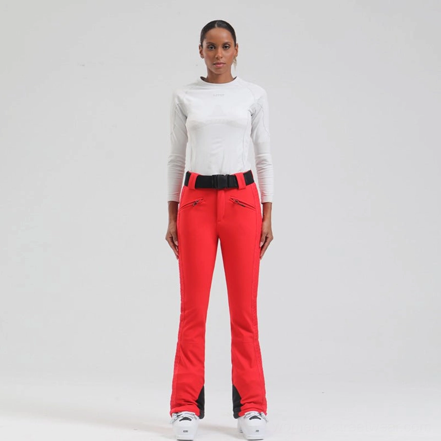 Red women's flared ski pants with black heel patches, waterproof zip pockets, adjustable belt, and technical streetwear design
