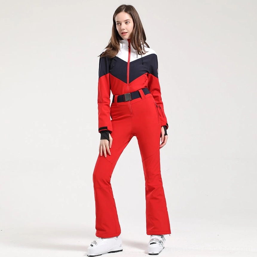 Women's red white navy colorblock ski jumpsuit shown in a full front view with flared red trousers black waist belt and white ski boots