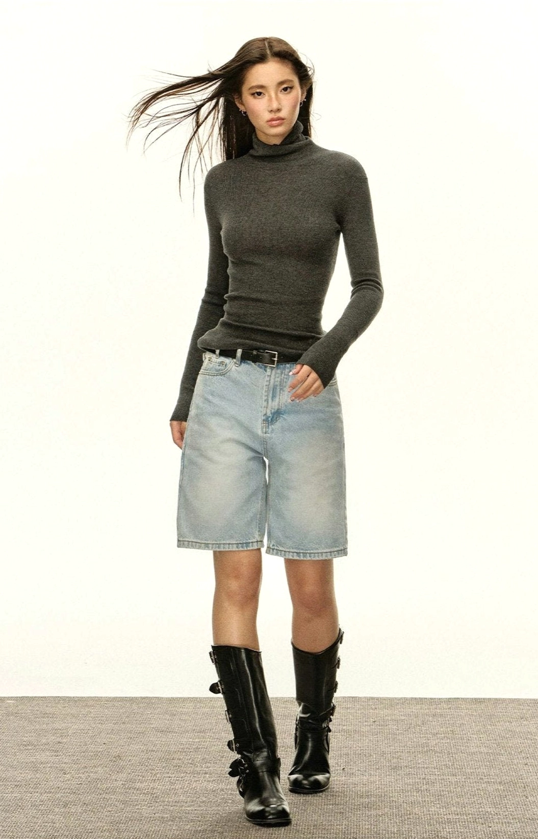Women's grey ribbed turtleneck slim-fit sweater styled with denim shorts and black boots