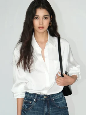 Pearl white women's satin draped pocket shirt styled with high waisted jeans and a black shoulder bag in a relaxed Korean streetwear outfit