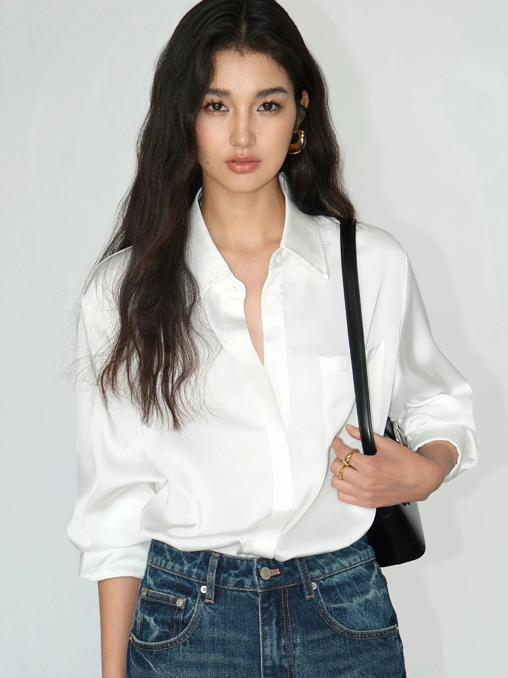 Pearl white women's satin draped pocket shirt styled with high waisted jeans and a black shoulder bag in a relaxed Korean streetwear outfit