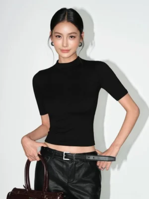 Women's black slim-fit mock neck knit crop tee three-quarter front view styled with leather pants and tote bag