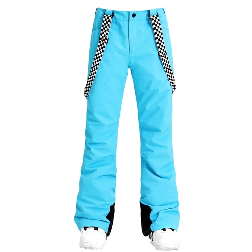 Women's sky blue checkerboard snow pants with flared ski streetwear legs, decorative suspenders, black ankle patches, and white snow shoes