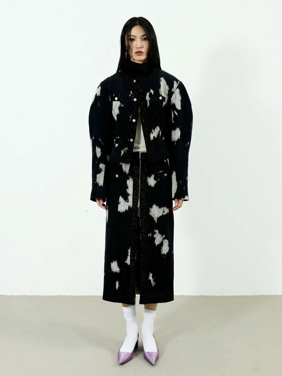 Front view of women's speckled corduroy midi skirt styled with a cropped jacket, black turtleneck, white socks, and purple heels