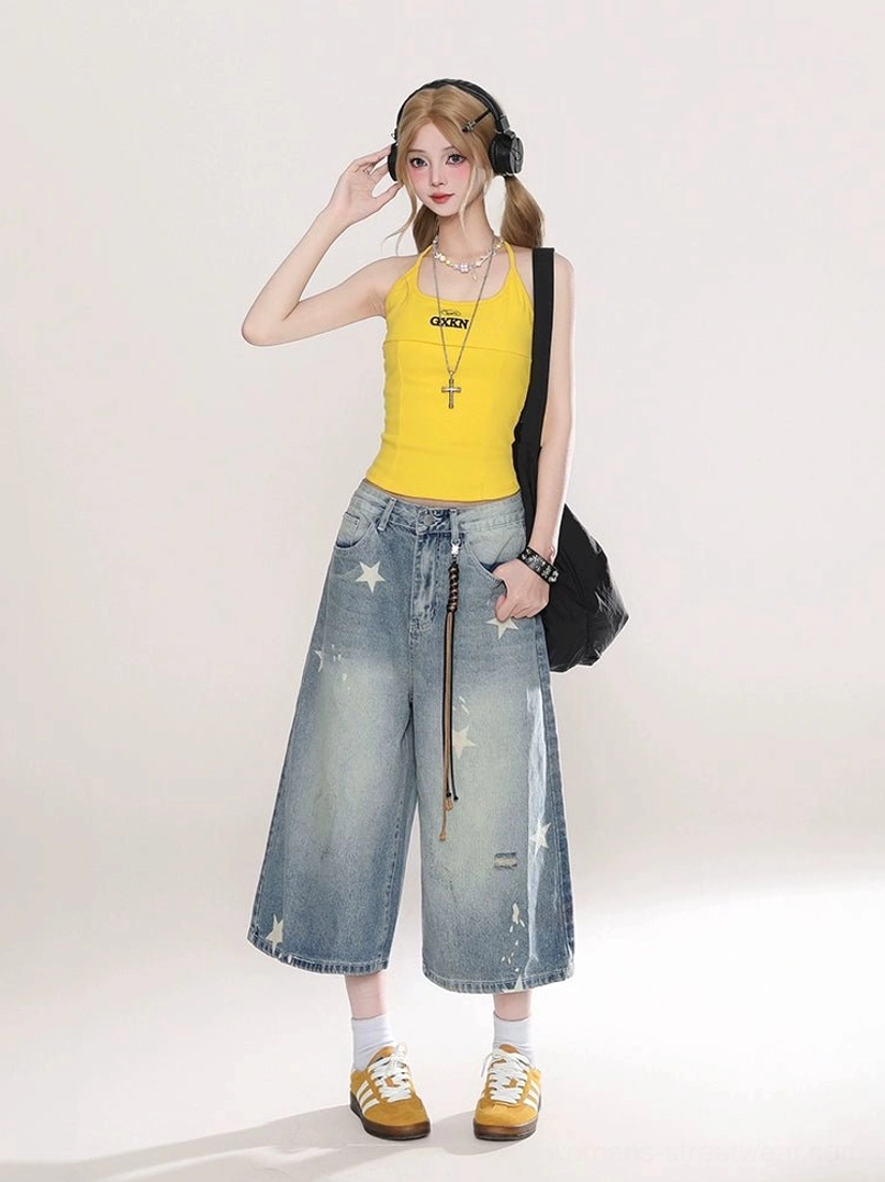 Female model wearing blue star print wide leg cropped jeans with yellow tank top and sneakers