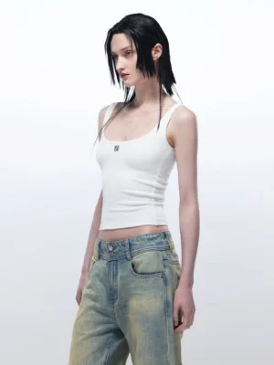 White slim fit U-neck streetwear tank top with metal chest badge side three-quarter view with yellow washed denim