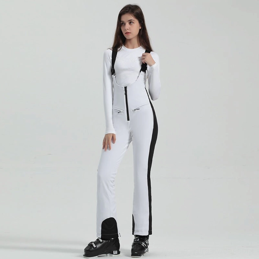 Women's white and black bib ski overalls with contrast side stripe panels, slim flared legs, front zipper, and ski boots