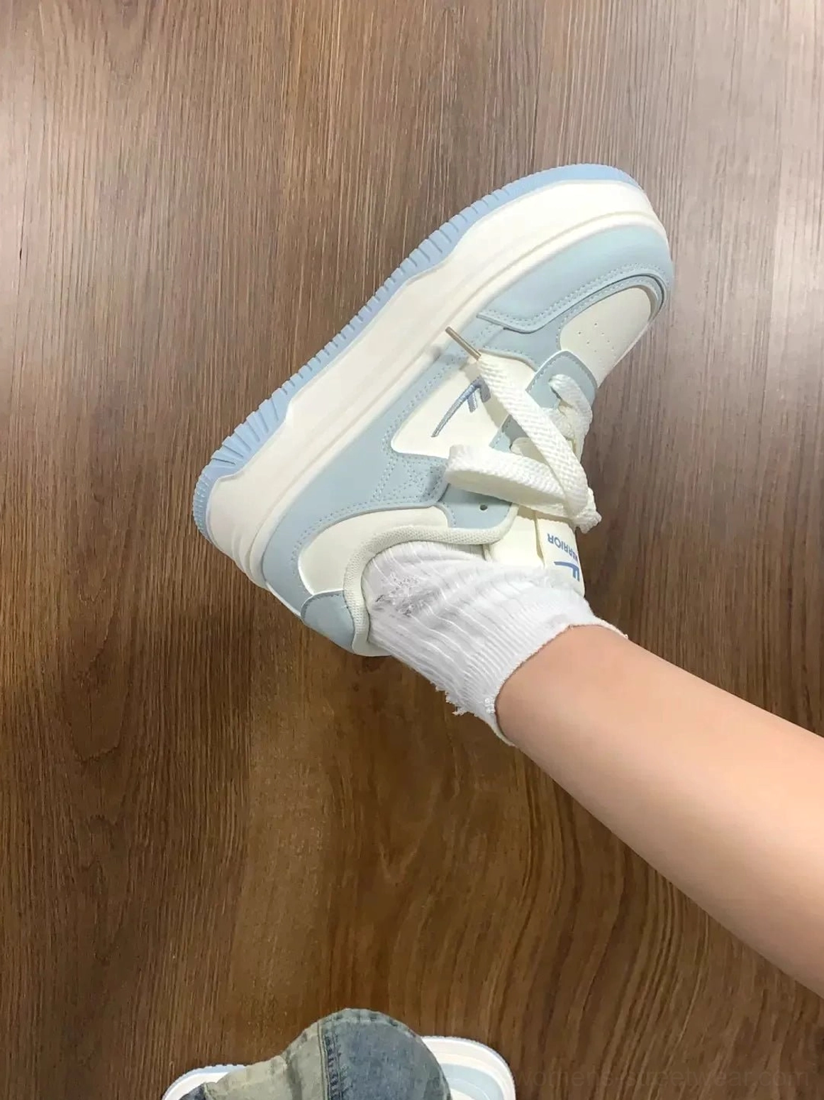 Hand-held view of women's white and blue platform sneaker showing stitched side panels and raised sole