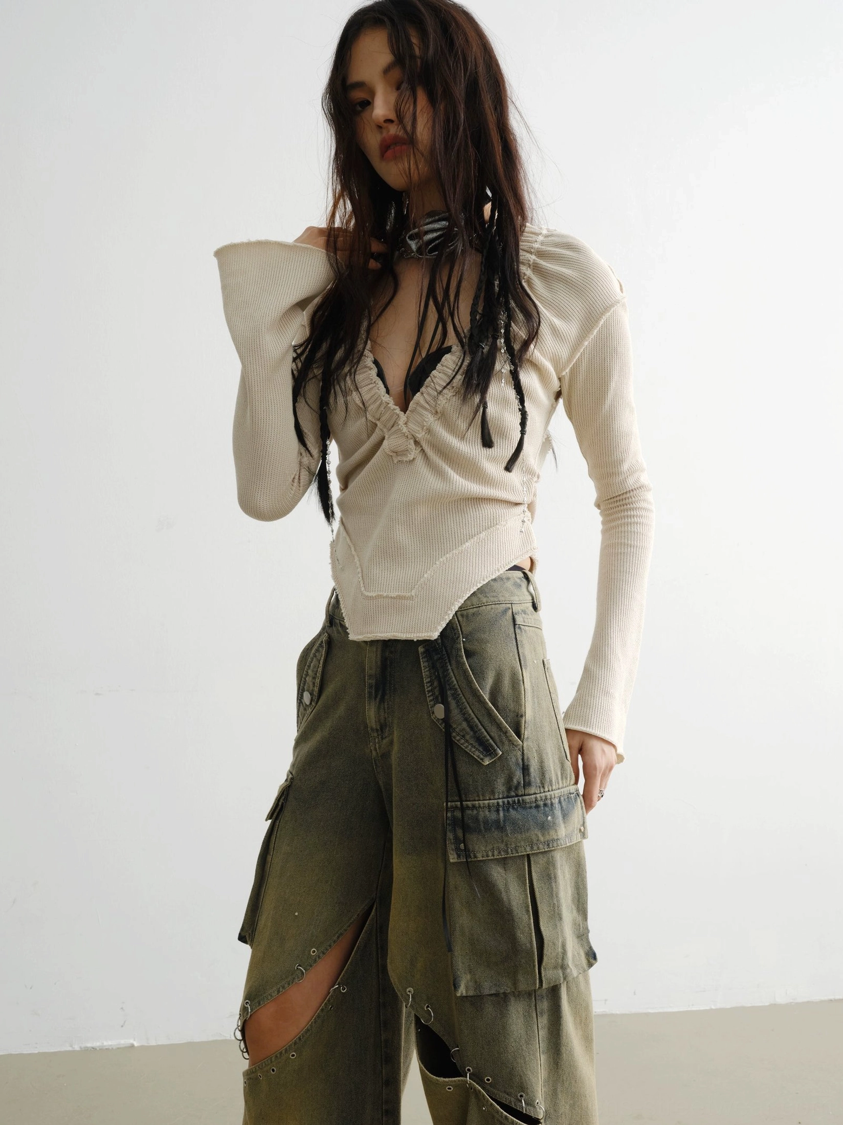 Three-quarter view of womens white deep V knit streetwear top showing fine neckline stitching, flared sleeves, and cargo denim styling