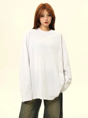 Female model wearing a white oversized long sleeve crew neck tee with drop shoulders and vintage washed wide leg jeans in a Korean streetwear studio outfit