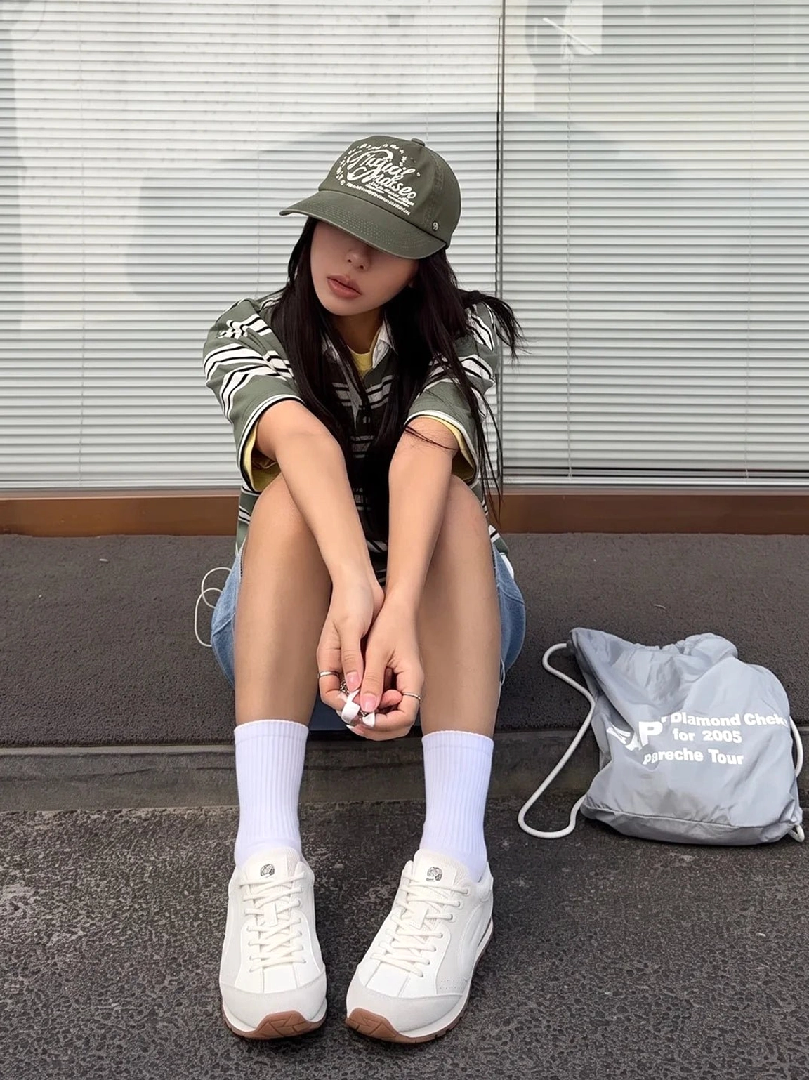 Women's gray white retro court sneakers with wing side panels and brown gum outsole worn in a seated streetwear outfit
