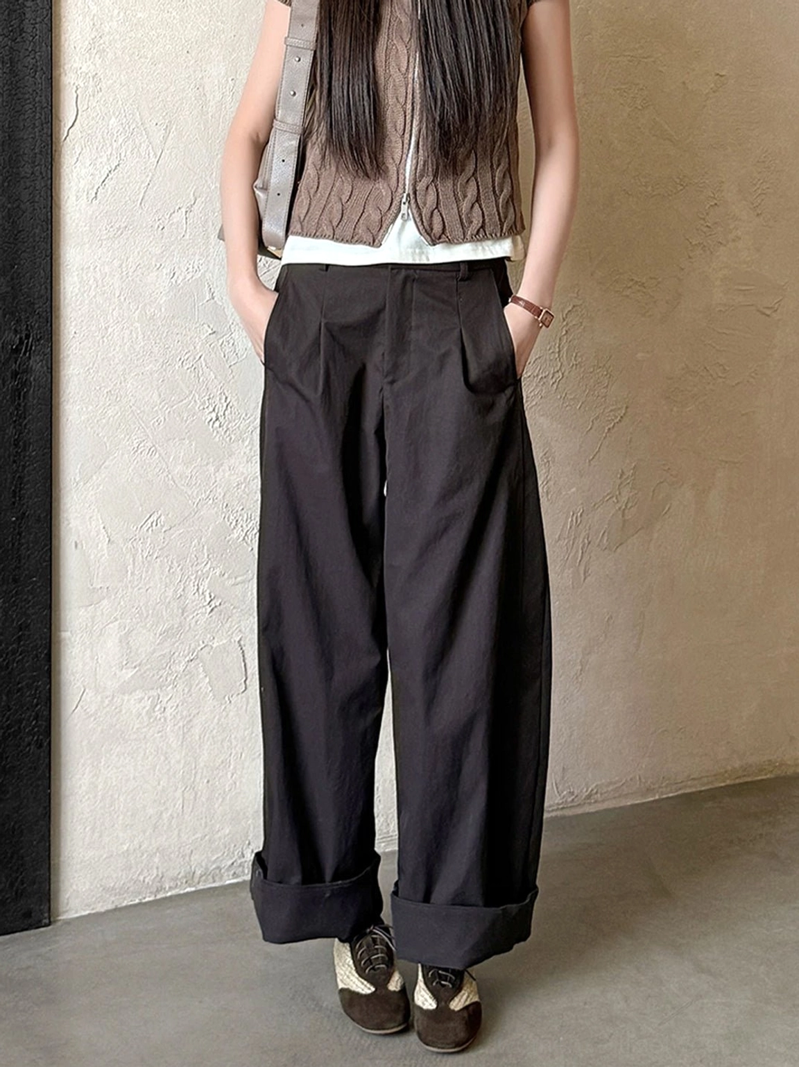 Woven leather German trainer sneakers paired with a brown knit vest, white tank top, and rolled black wide-leg trousers