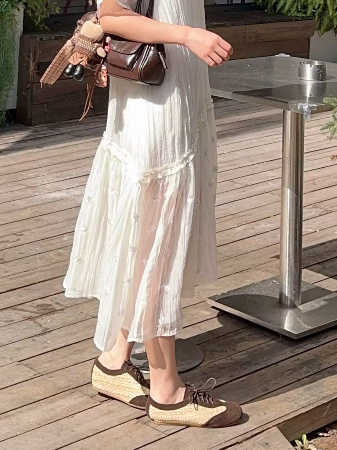 Low-angle view of woven leather German trainer sneakers worn with a flowing white midi dress and brown leather crossbody bag