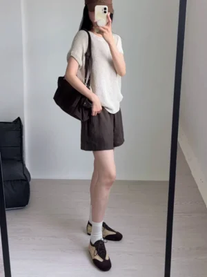Female streetwear outfit wearing woven leather German trainer sneakers with a knit top, brown shorts, and white crew socks in a casual indoor setting