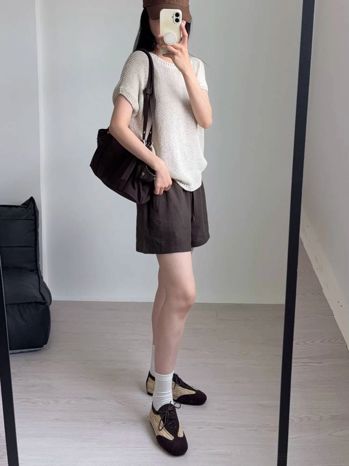 Female streetwear outfit wearing woven leather German trainer sneakers with a knit top, brown shorts, and white crew socks in a casual indoor setting