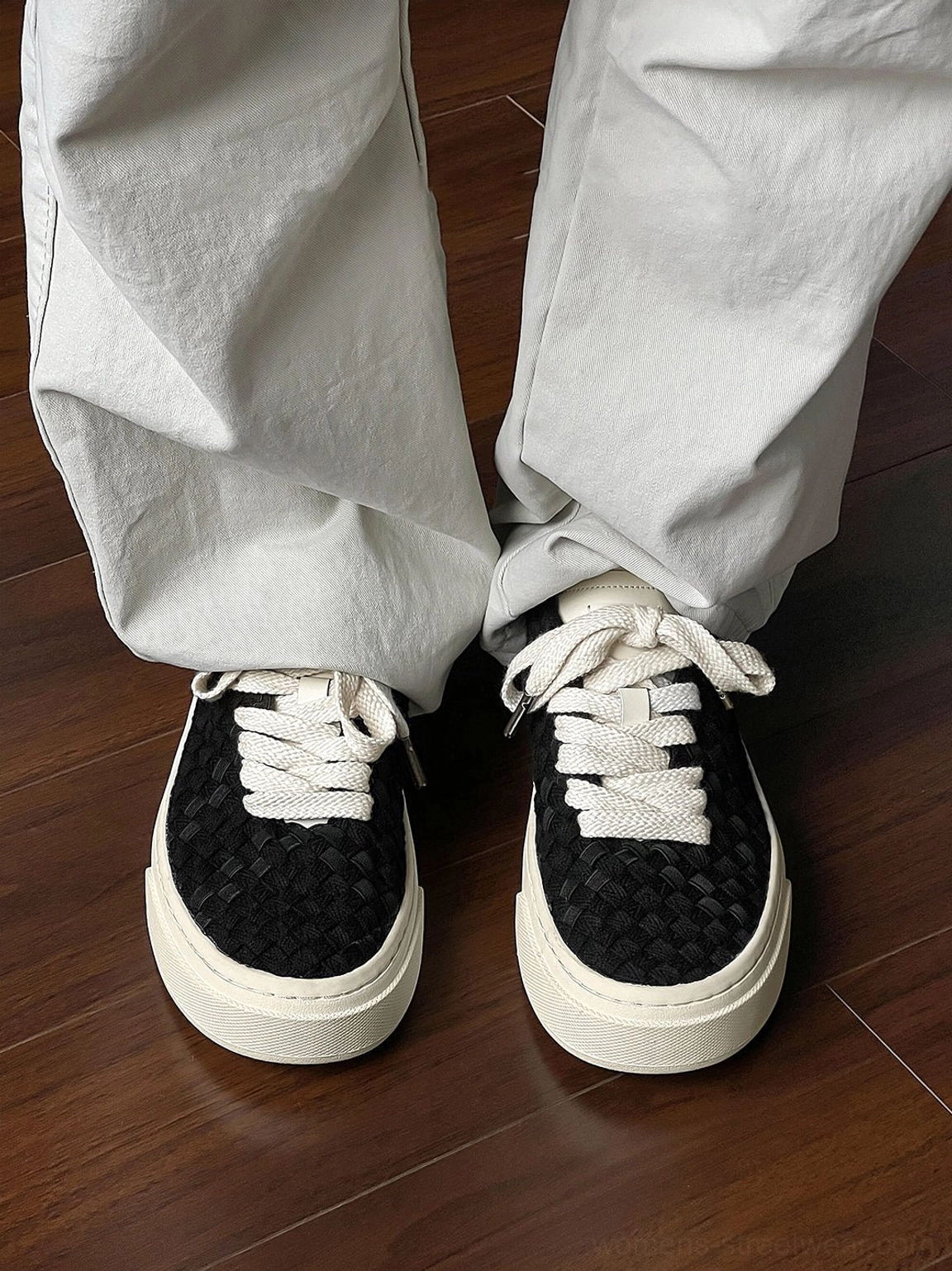Front close-up of black woven platform sneakers with wide flat laces and thick off-white sole