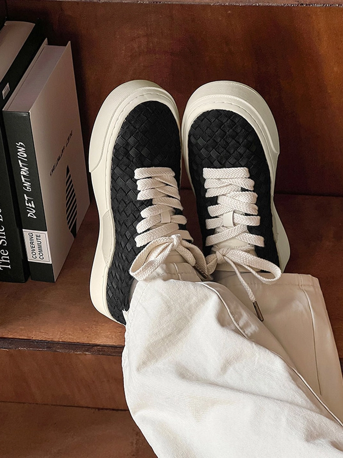 Top-down view of black woven platform sneakers worn with gray pants showing braided upper texture