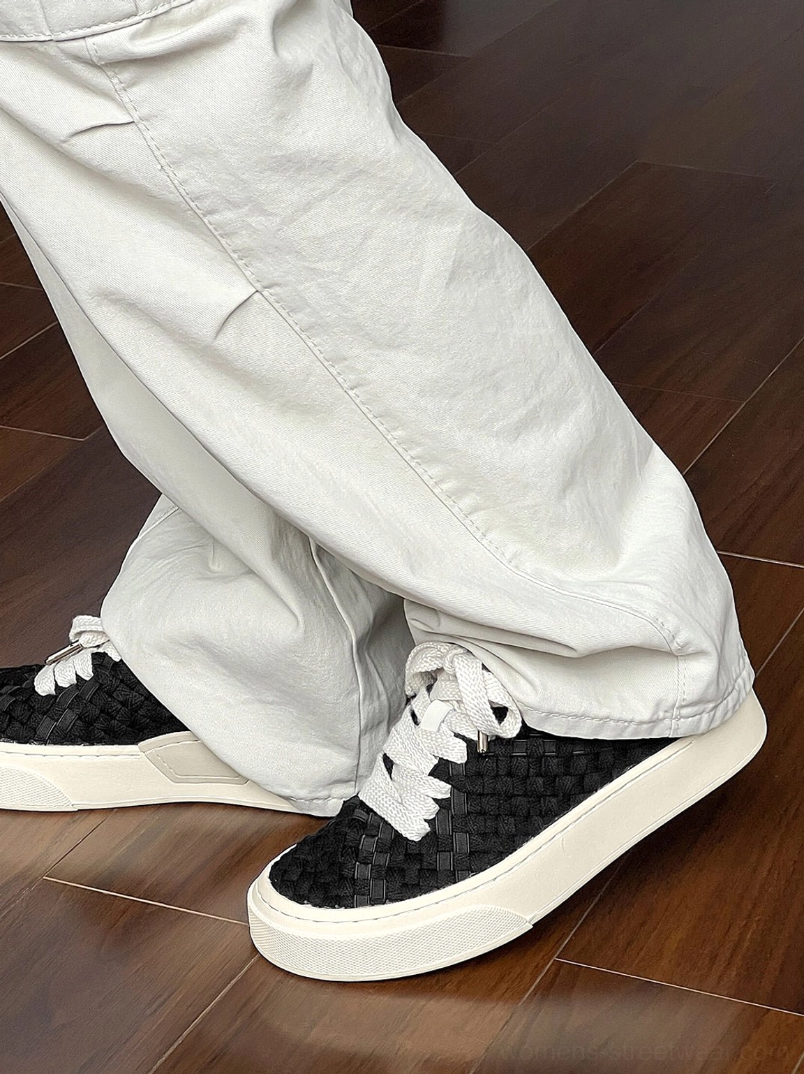 Black woven platform sneakers worn with light gray wide-leg pants in a casual streetwear outfit