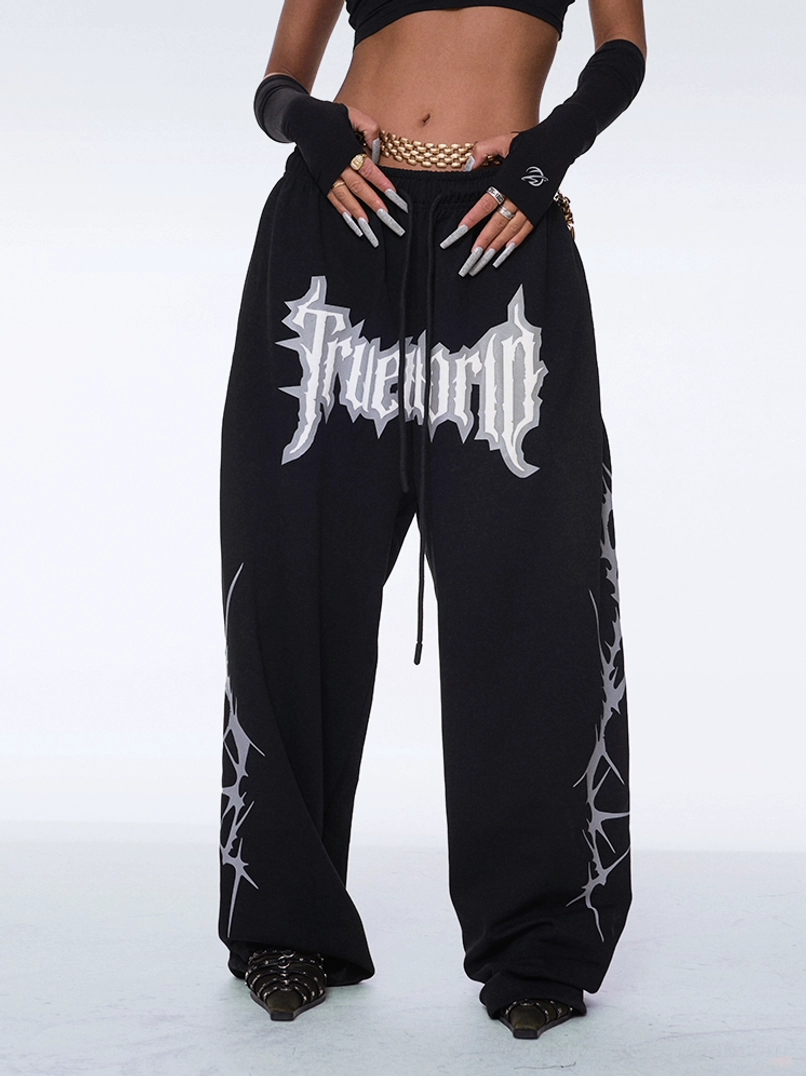 Y2K gothic streetwear pants shown from the front with ultra-baggy wide-leg silhouette, drawstring waist, bold graphic print, and sharp thorn side artwork